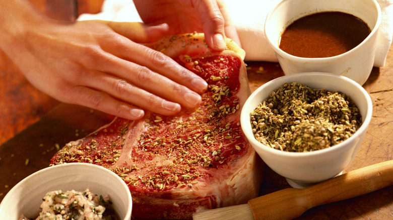 Person seasoning steak with hand