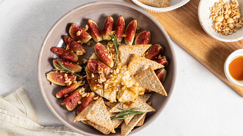 Plate with hazelnuts and fresh slices of figs, baked Brie, and crackers.