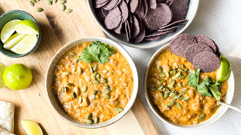 Hearty white chicken and navy bean chili in bowls with blue corn tortilla chips, pepitas, and lime wedges