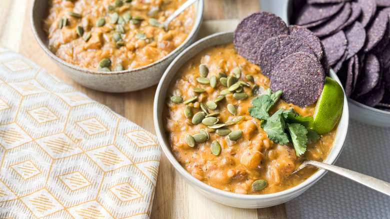 Hearty white chicken and navy bean chili with pepitas, cilantro and blue corn tortilla chips in bowls