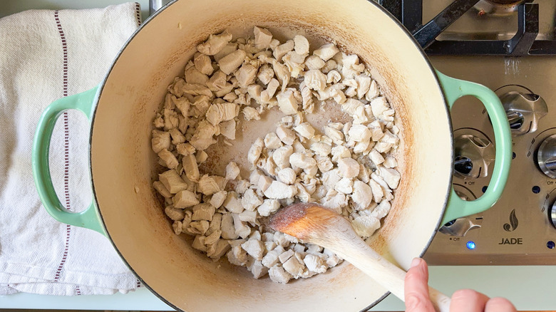 Sauteing cubed chicken in large pot with wooden spoon on stovetop