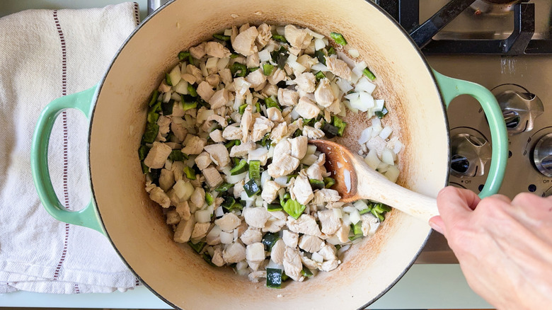 Chopped chicken, poblano peppers, and yellow onion in large pot on stovetop with wooden spoon