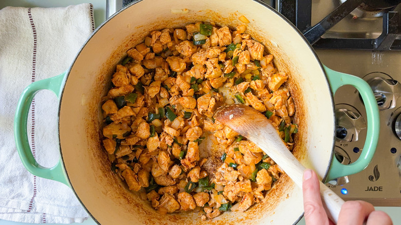 Sauteing chopped chicken, poblano peppers, yellow onion, and spices with wooden spoon in large pot on stovetop