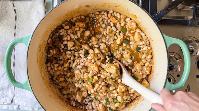 Stirring white chicken and navy bean chili with wooden spoon in large pot on stovetop