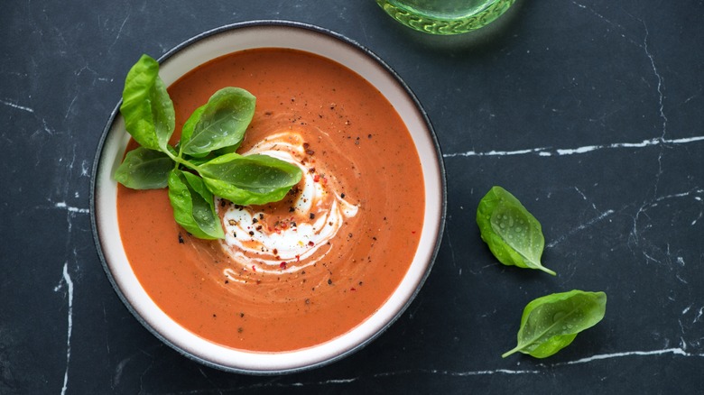 A bowl of tomato soup with a swirl of cream, black pepper, and fresh basil leaves