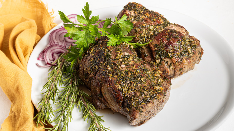 Herb-roasted beef tenderloin on a plate with fresh herbs and sliced red onion 
