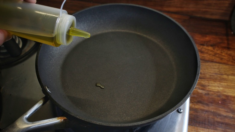 hand adding oil to skillet