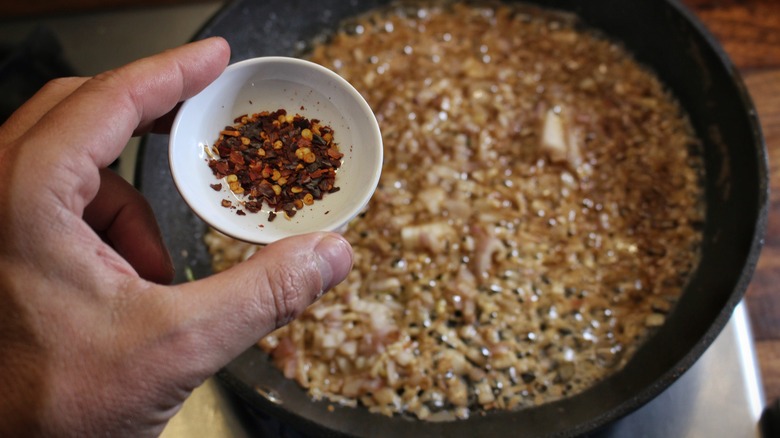 adding crushed red pepper to skillet