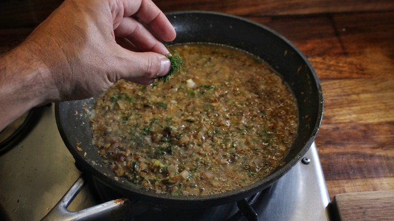 hand adding dill fronds to skillet of sauce