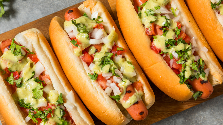 Three hot dogs with onions, avocado salsa, and cilantro