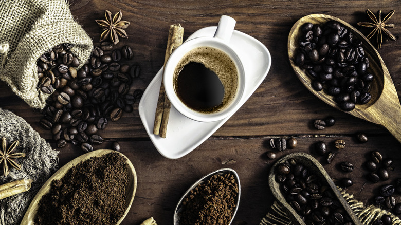 Cup of coffee surrounded by various spices and beans in scoops and bags