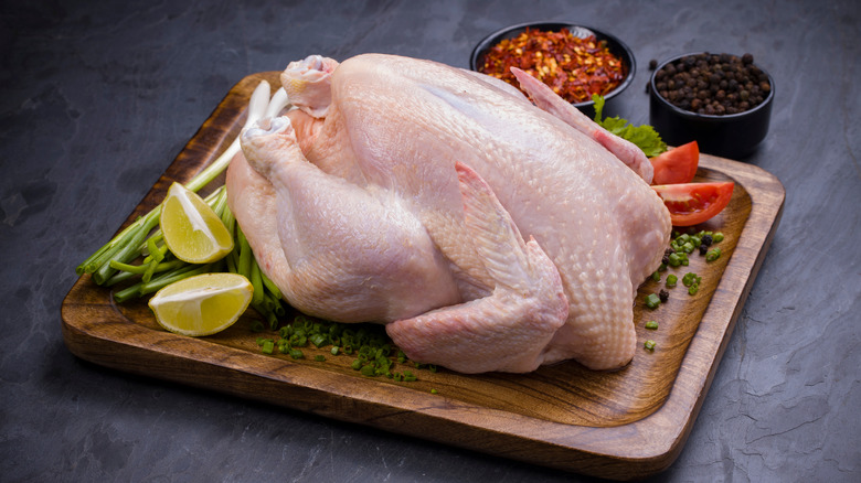 Whole raw chicken and aromatics on cutting board