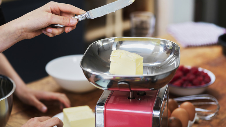 Hand cutting pieces of butter and putting them on a kitchen scale