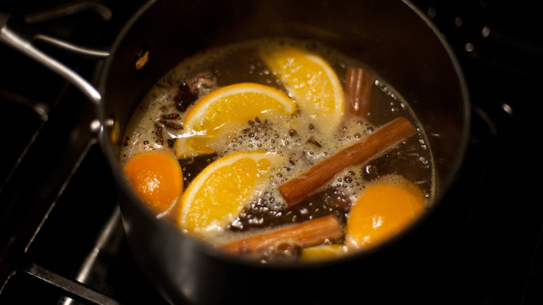 a pot of simmering liquid with oranges, cloves, and cinnamon sticks