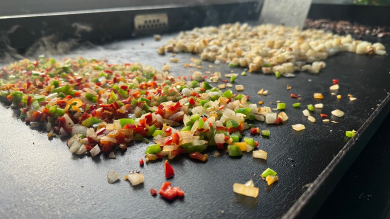 chopped veggies and potatoes cooking on a griddle