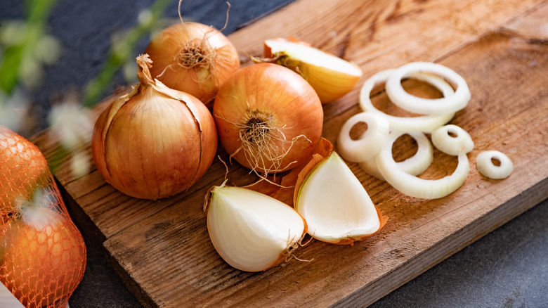 Whole and sliced yellow onions on a cutting board