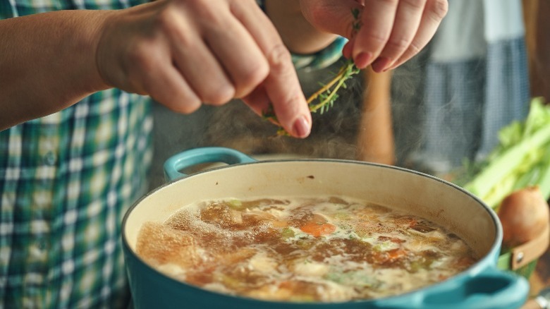 Woman putting thyme into a Dutch oven of chicken stock