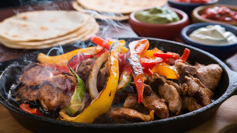 Sizzling steak for fajitas, with tortillas and condiments in the background.