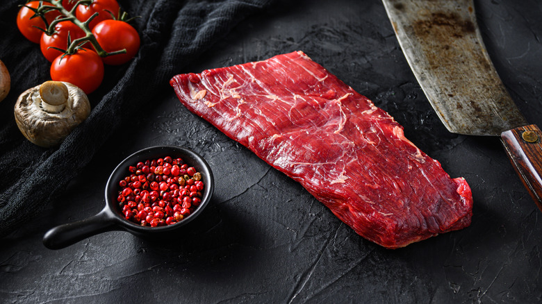 A deep red flap steak is raw beside a cleaver in a stylishly industrial setting.