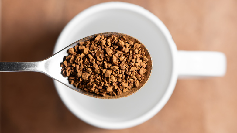 A spoonful of instant coffee held over a white mug