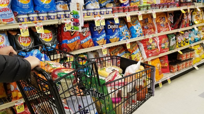 Person pushes a shopping cart down the junk food aisle