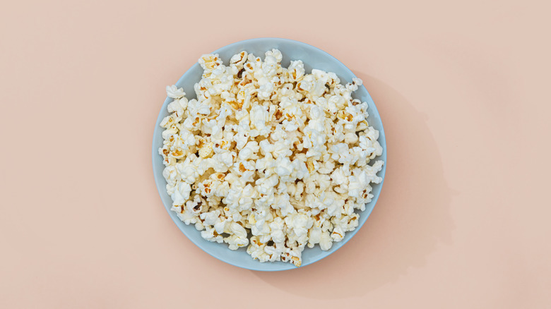 This aerial view shows a light blue bowl of popcorn on a peach background.