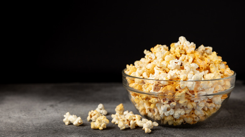 A clear bowl is overflowing with popcorn and set on a black background..