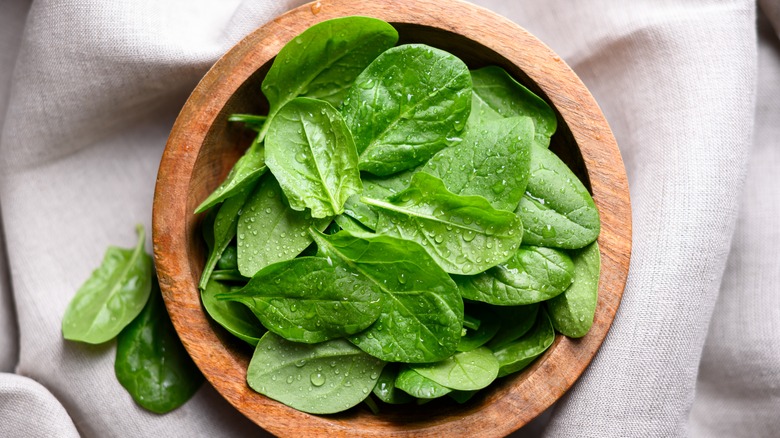 Spinach leaves with water drops in a wooden bowl sitting on a linen tablecloth