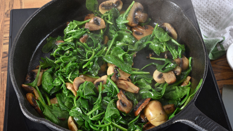 A cast iron frying pan with cooked spinach and mushrooms inside