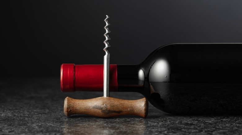 A corkscrew next to a bottle of red wine