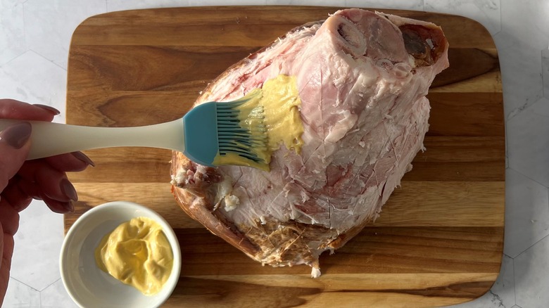 hand brushing mustard on ham