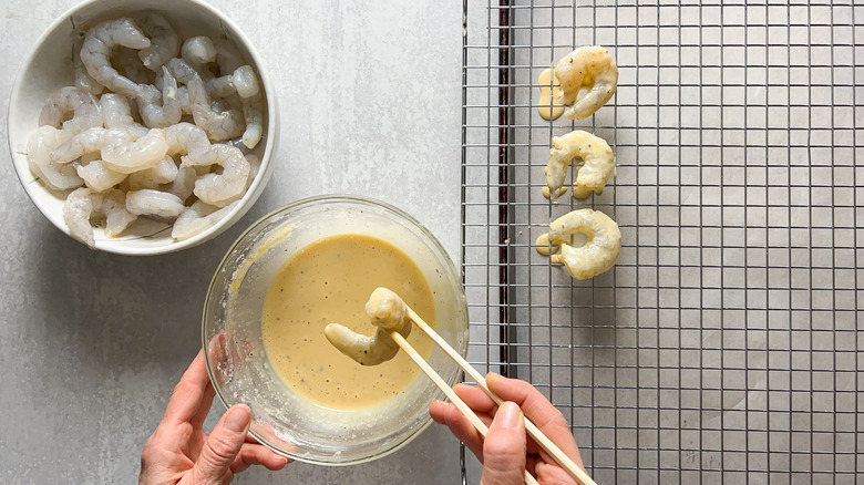 Dipping shrimp in batter with chopsticks and placing on rack over pan