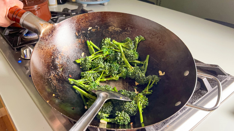 Broccolini, garlic, and red pepper flakes cooking in wok on stove top