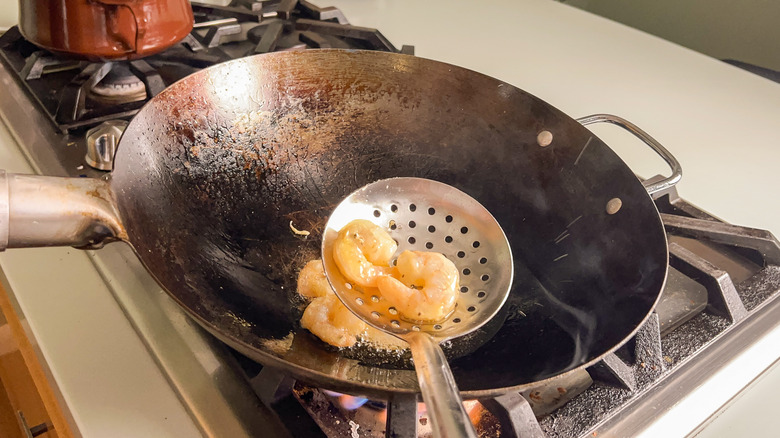 Removing shrimp from hot oil in wok