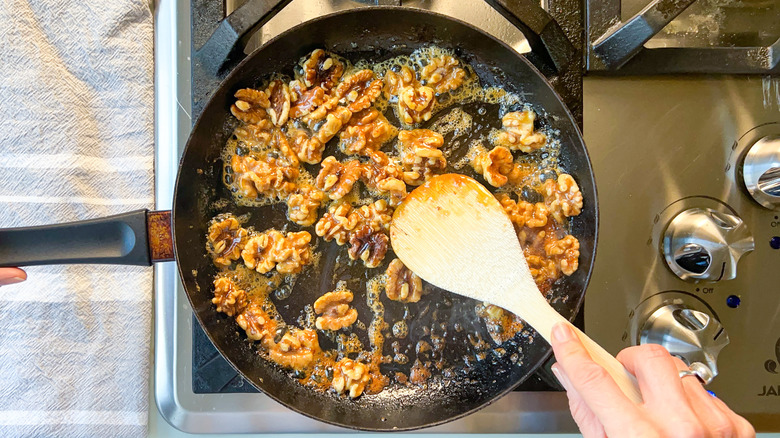 Stirring walnuts and honey in skillet on stove top