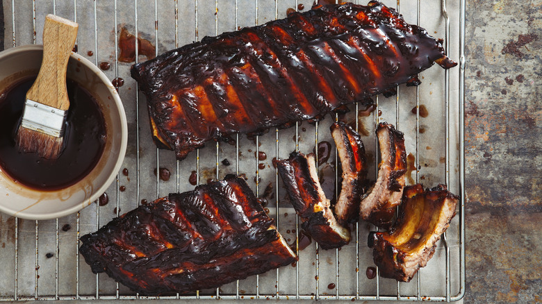 A bowl of barbecue sauce sits beside prepared ribs.