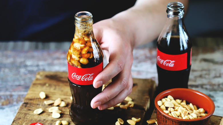 hand holding bottle of coke with peanuts inside