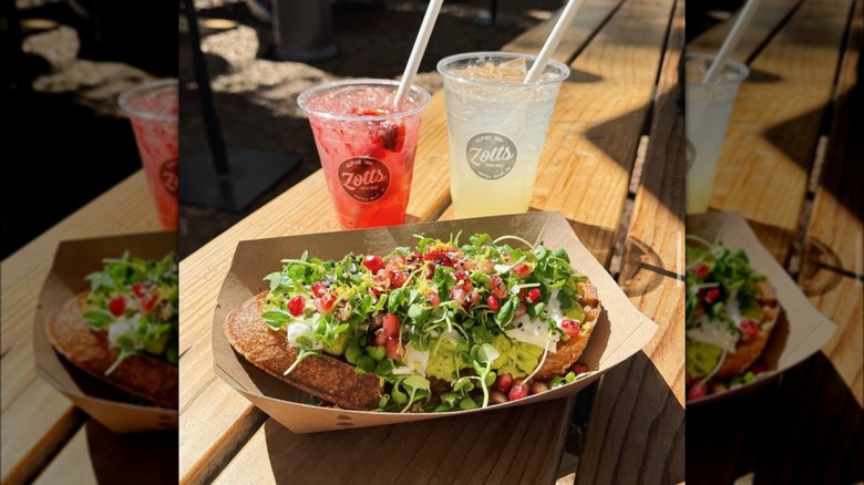 Two Zott's drinks and a burrata pomegranate avocado toast on a picnic table