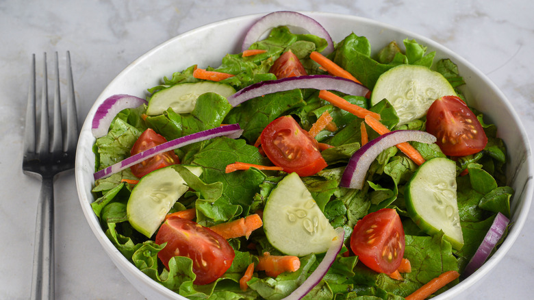 A crisp salad sits in a white bowl with a fork next to it.