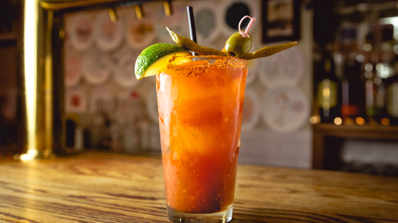 A Bloody Mary on a table garnished with lime, olive, and pepper