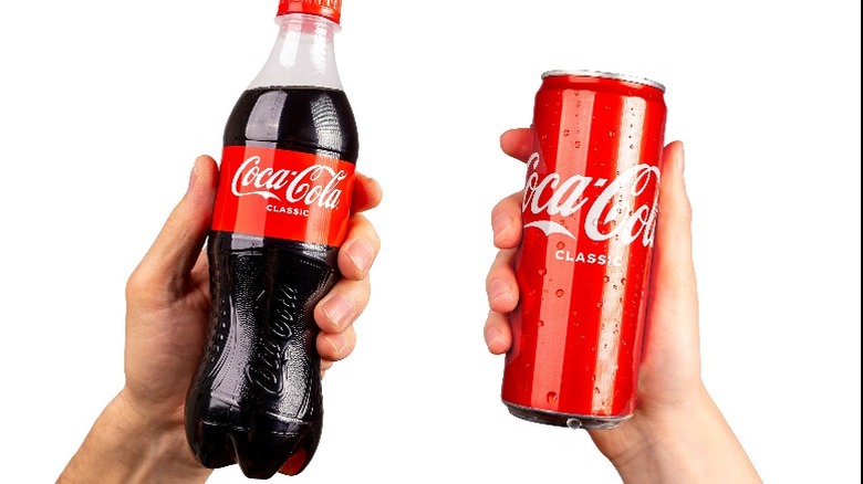 Hands hold a bottle and can of Coke side-by-side for comparison