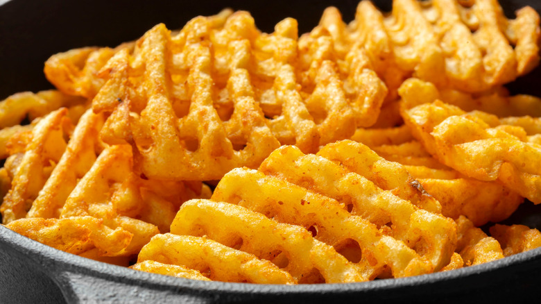 Close-up of cooked, seasoned waffle fries in a cast-iron skillet