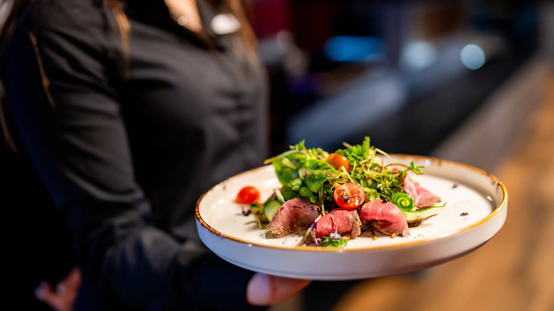 A restaurant server carrying a plate of seared tuna