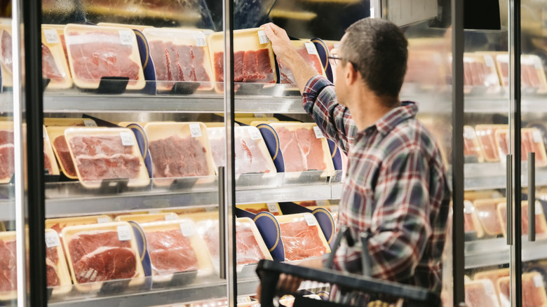 Customer taking meat from supermarket refrigerator