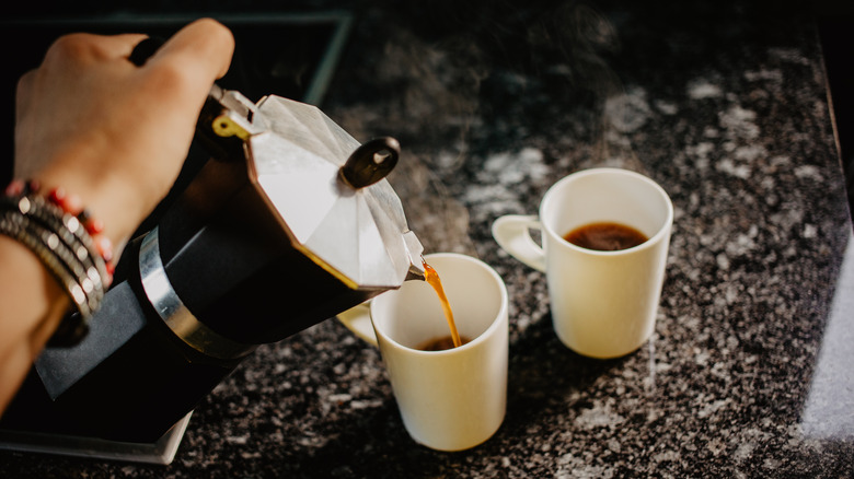 Hand pours coffee into two mugs