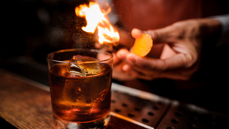 Bartender lighting a flaming cocktail, holding a piece of citrus zest as a garnish