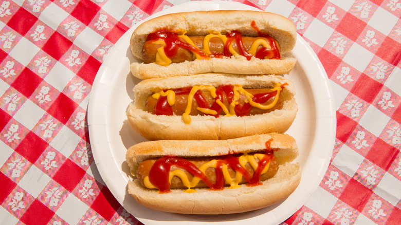 3 hot dogs with mustard and ketchup on picnic table.