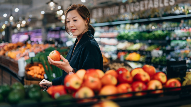 Woman shopping in the produce aisle holding an apple