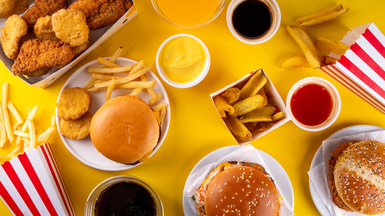 Fast food burgers, fries, chicken nuggets, and sauces on a yellow background