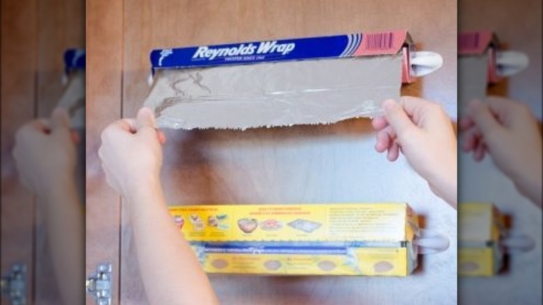 Person pulling aluminum foil secured to the wall with Command Hooks